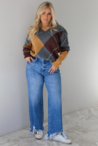Woman wearing a patterned sweater and blue jeans. The photo is taken indoors against a white wall with white marble flooring. 