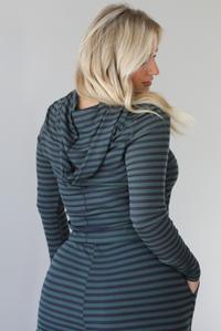 Woman wearing a navy and olive striped patterned set featuring a hoodie top and high waisted pants. The photo is taken indoors against a white wall. The photo shows a closeup of the back of the hoodie. 