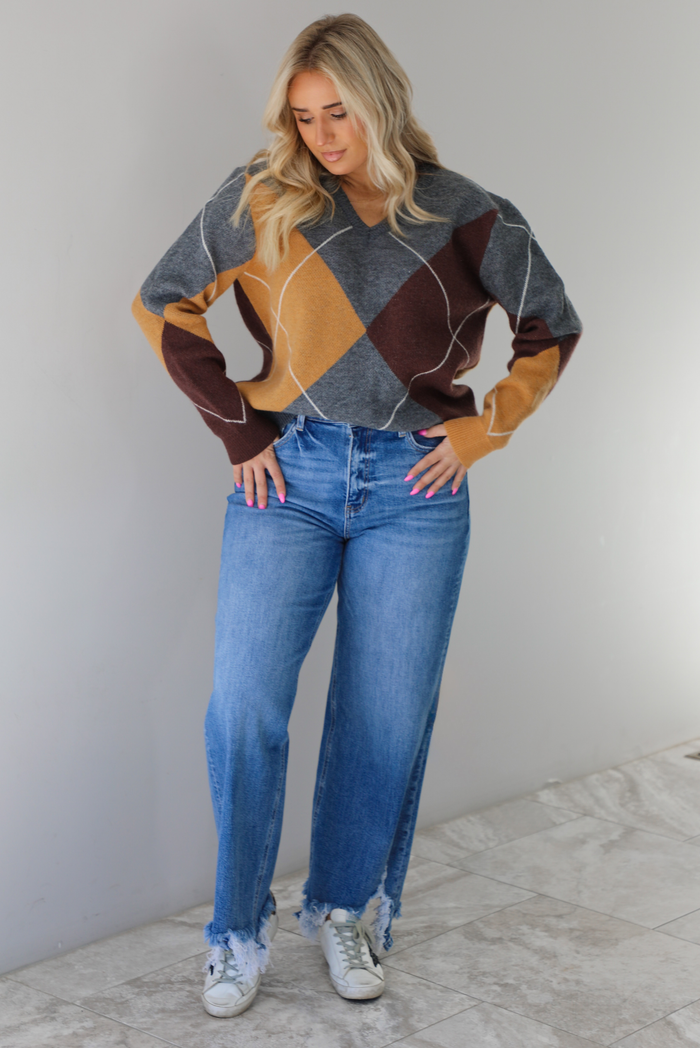Woman wearing a patterned sweater and blue jeans. The photo is taken indoors against a white wall with white marble flooring. 