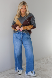 Woman wearing a patterned sweater and blue jeans. The photo is taken indoors against a white wall with white marble flooring. 