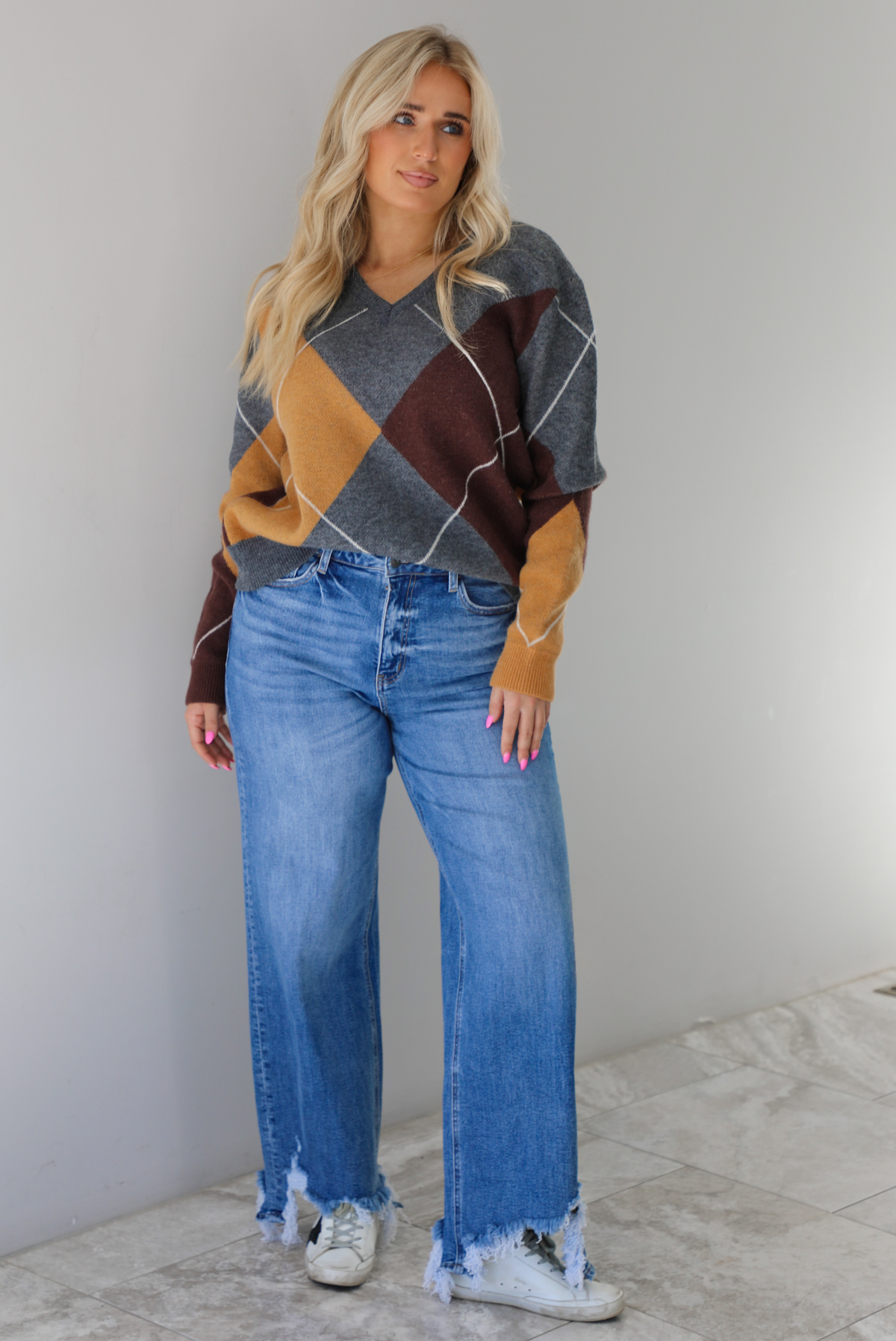 Woman wearing a patterned sweater and blue jeans. The photo is taken indoors against a white wall with white marble flooring. 