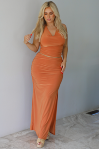 Woman wearing an orange halter neck and maxi-length skirt indoors against a white wall with white marble flooring. 