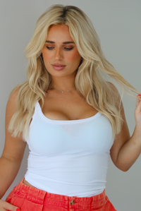 Woman wearing a white tank top and red shorts indoors against a white wall. The photo shows a closeup of the tank, which has a ribbed textured material. 