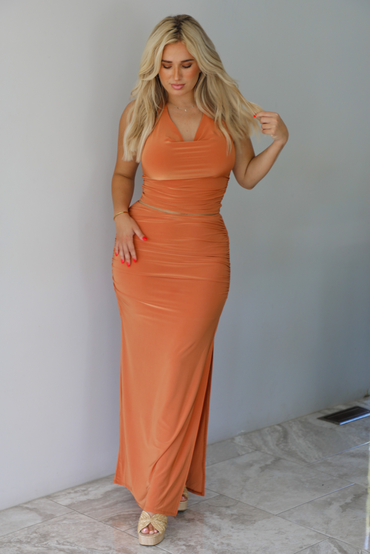 Woman wearing an orange halter neck and maxi-length skirt indoors against a white wall with white marble flooring. 
