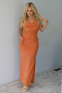 Woman wearing an orange halter neck and maxi-length skirt indoors against a white wall with white marble flooring. 