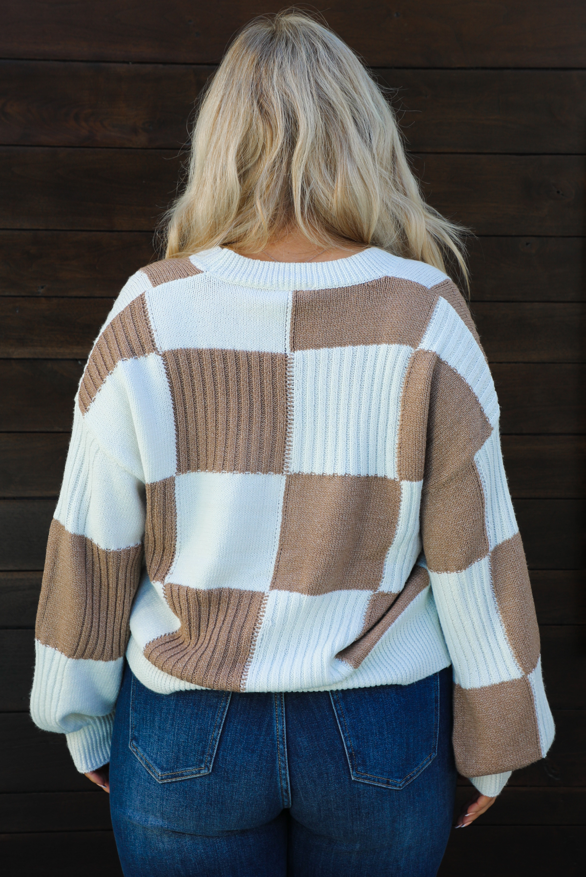 Close up of the back of a woman model wearing a white and tan checkered patterned cardigan and dark wash denim. The cardigan has functional button closures in the front, is lightweight, and has a relaxed fit. 