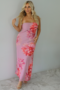 A woman modeling a strapless mauve maxi dress with a large red and orange floral print, standing indoors against a white wall with white marble flooring. 