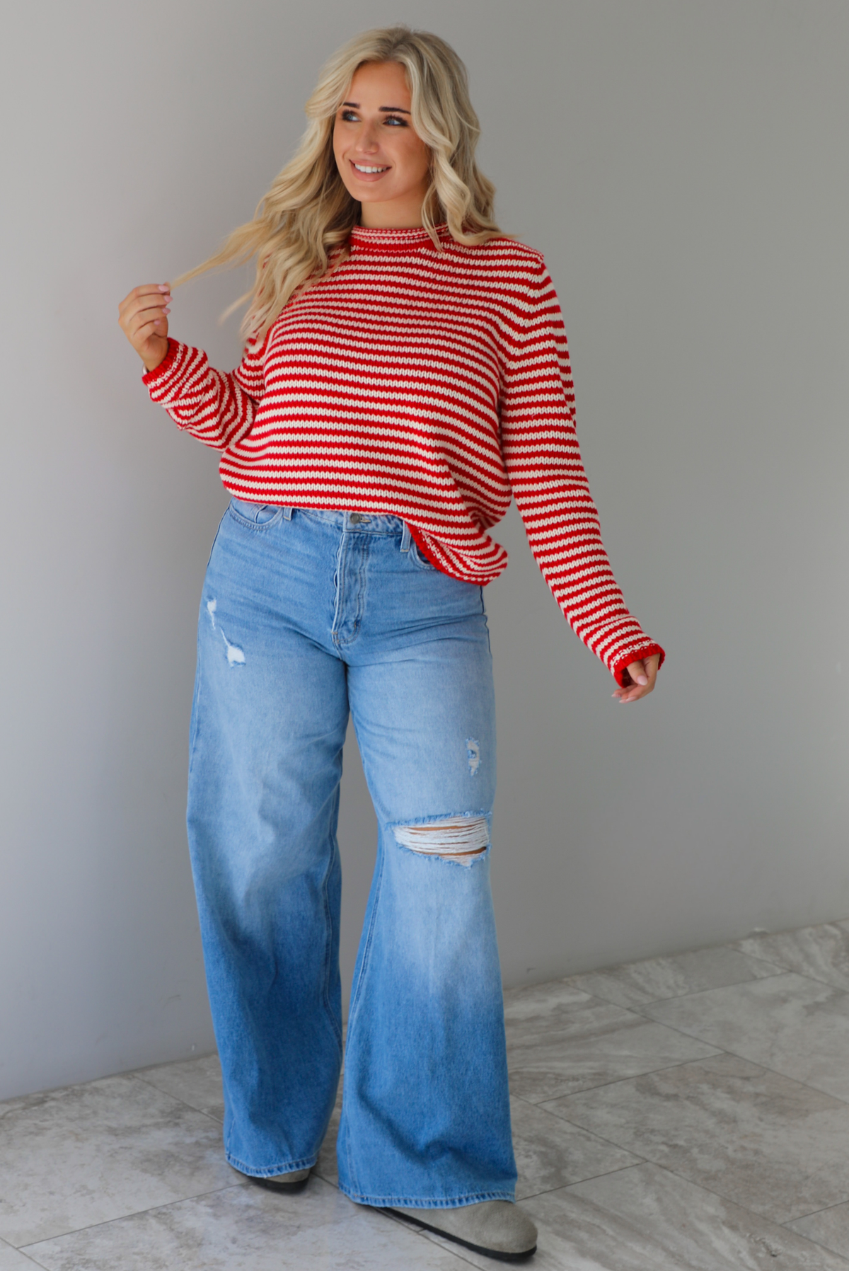 Woman wearing a red and white striped sweater with high waisted medium wash flared hem denim. The photo is taken in front of a white wall with white marble flooring. 