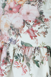 Woman wearing a cream and multi-colored floral skirt that has a high waistline and a shorter length. The photo shows a closeup of the pattern and colored of the skirt, which displays a white variety of flora patterns with branches and birds.