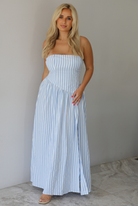 Woman wearing a blue and white striped strapless maxi dress indoors against a white wall with white marble flooring.