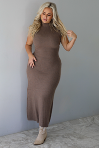 A woman wearing a mocha sleeveless knit maxi dress, standing indoors against a white wall with white marble flooring. 