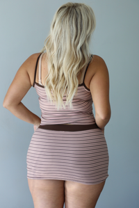 A woman shown from behind wearing a pink and brown striped two piece matching set consisting of a tank top and mini skirt with a thick brown waistband, standing indoors against a white wall.