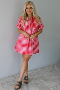Woman wearing a pink and red gingham collared neckline t-shirt dress indoors against a white wall with white marble flooring. 