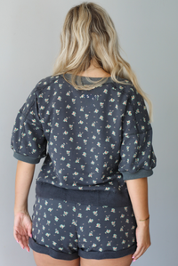 Woman wearing a charcoal with a multi-colored floral two piece set featuring an oversized top with puffed sleeves and shorts indoors against a white wall. The photo shows a close up of the back of the set. 
