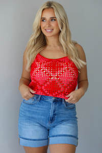 Woman wearing a pink and red loose knit crochet cropped top with light wash denim shorts indoors against a white wall.