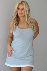 Woman wearing a heather grey athleisure dress with white trim detailing at the hem indoors against a white wall.