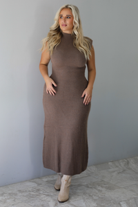 A woman wearing a mocha sleeveless knit maxi dress, standing indoors against a white wall with white marble flooring. 