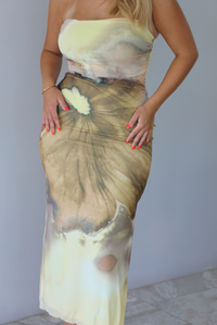 Woman wearing a yellow and brown floral print, strapless, fitted midi dress indoors against a white wall. The photo shows a closeup of the dress. 