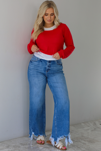 Woman wearing a red and white layered appearance top with dark wash denim jeans. The photo is taken indoors against a white wall with white marble flooring. 