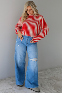 Woman wearing a red and white striped sweater with high waisted medium wash flared hem denim. The photo is taken in front of a white wall with white marble flooring. 