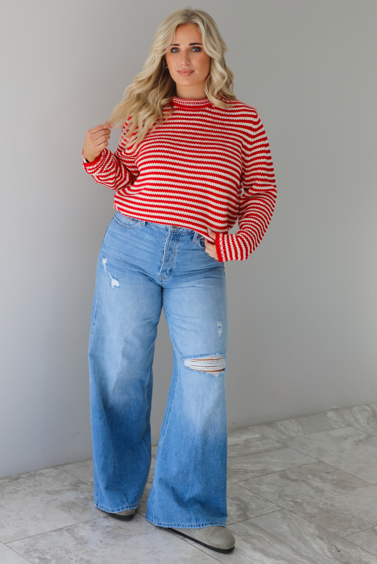 Woman wearing a red and white striped sweater with high waisted medium wash flared hem denim. The photo is taken in front of a white wall with white marble flooring. 