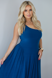 Woman wearing a blue one strap maxi dress indoors against a white wall. The photo shows a closeup of the bodice of the dress. 