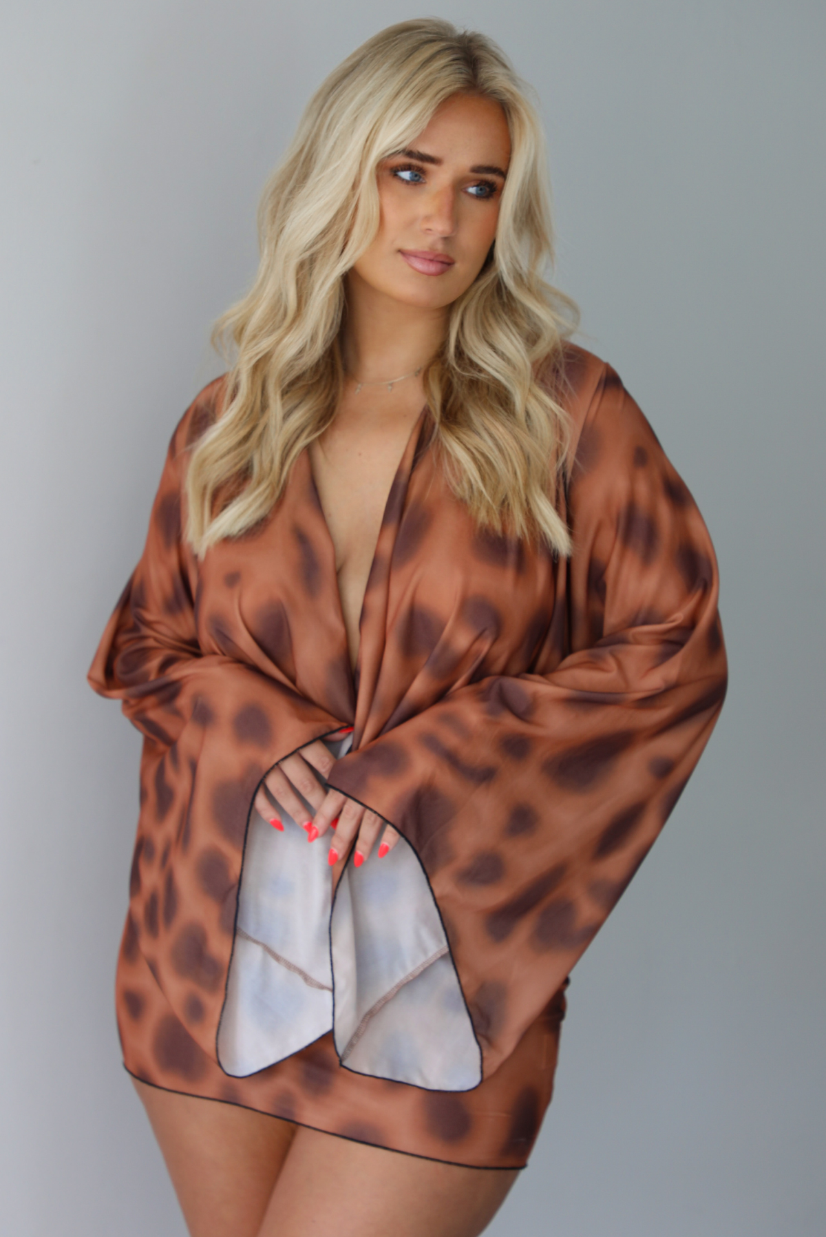 Woman wearing a brown and ruse mini dress that has a very low slouched cowl-neck design, long sleeves, and is fitted at the hips indoors against a white wall.