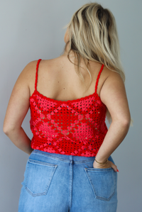 Woman wearing a pink and red loose knit crochet cropped top with light wash denim shorts indoors against a white wall. The photo shows the back of the top. 