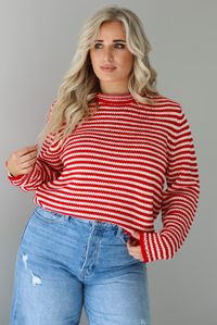 Woman wearing a red and white striped sweater with high waisted medium wash flared hem denim. The photo shows a closeup of the sweater which has a front tuck. The photo is taken in front of a white wall.