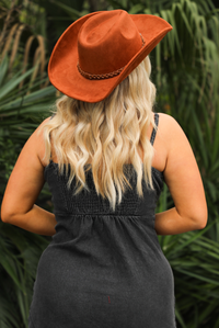 Woman wearing a black denim maxi length dress that has thin, adjustable spaghetti straps, cup stitching at the bust with other stitched details, slight distressing at the thighs, functional button closures in the front, with a heavier weight material with some stretch throughout, smocked material in the back, and is not lined. The photo shows a close up of the back of the dress which has a smocked portion at the top of the back and the adjustable straps. 