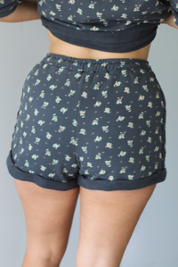 Woman wearing a charcoal with a multi-colored floral two piece set featuring an oversized top with puffed sleeves and shorts indoors against a white wall. The photo shows a closeup of the back of the shorts.