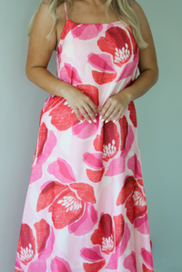 Woman wearing a pink and red floral print maxi dress with thin straps and a flowy fit indoors against a white wall and shows a closeup of the upper portion of the dress. 