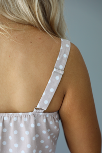 Woman wearing a to piece tan with white polka dots set featuring a cropped tank top and high waisted maxi length skirt. The photo is taken indoors against a white wall and shows a closeup of the back of the tank with its adjustable straps.