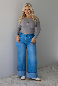 A woman wearing a striped, cropped long sleeved top with a beaded espresso martini on the front with medium wash denim jeans, standing indoors against a white wall with white marble flooring 