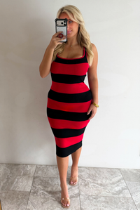 A woman taking a mirror selfie wearing a red and black striped body-con midi dress, paired with clear strapped heels, standing indoors against a white wall with white marble flooring. 