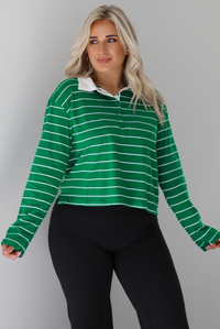Woman wearing a green with white striped collared cropped top with functional button closures a quarter at the top. The top is paired with black leggings. The photo is taken in front of a white wall.
