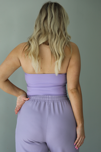 Woman wearing a two piece lavender set featuring a strapless, fitted tube top, and high waisted, flared hem pants. The photo is taken indoors against a white wall and shows a closeup of the back of the tube top, which has a ribbed texture.