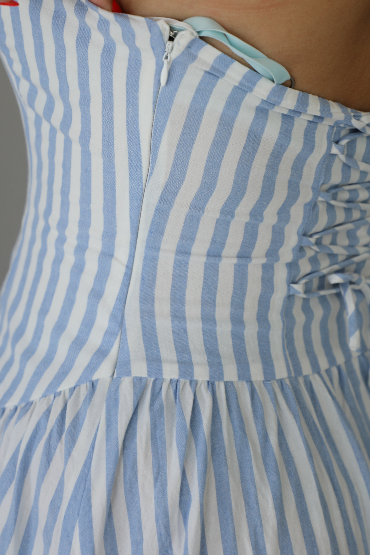 Woman wearing a blue and white striped strapless maxi dress indoors against a white wall. The photo shows a closeup of the side of the dress, which has a zipper closure. 