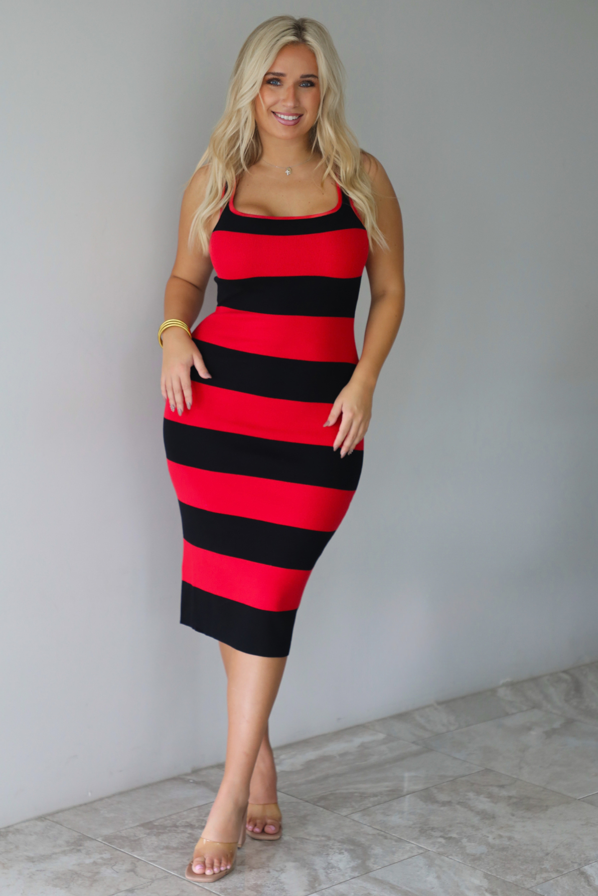 A woman wearing a red and black striped body-con midi dress standing indoors against a white wall with white marble flooring. 