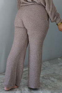 A woman shown from the waist down from behind wearing a mocha and white striped matching two piece set featuring a cropped, flowy. long sleeved top paired with high waisted wide leg pants, standing indoors against a white wall with white marble flooring. The photo shows a closeup of the back of the pants. 