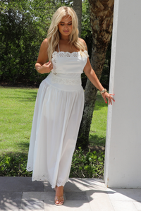 Woman in a white set standing outdoors with greenery in the background.