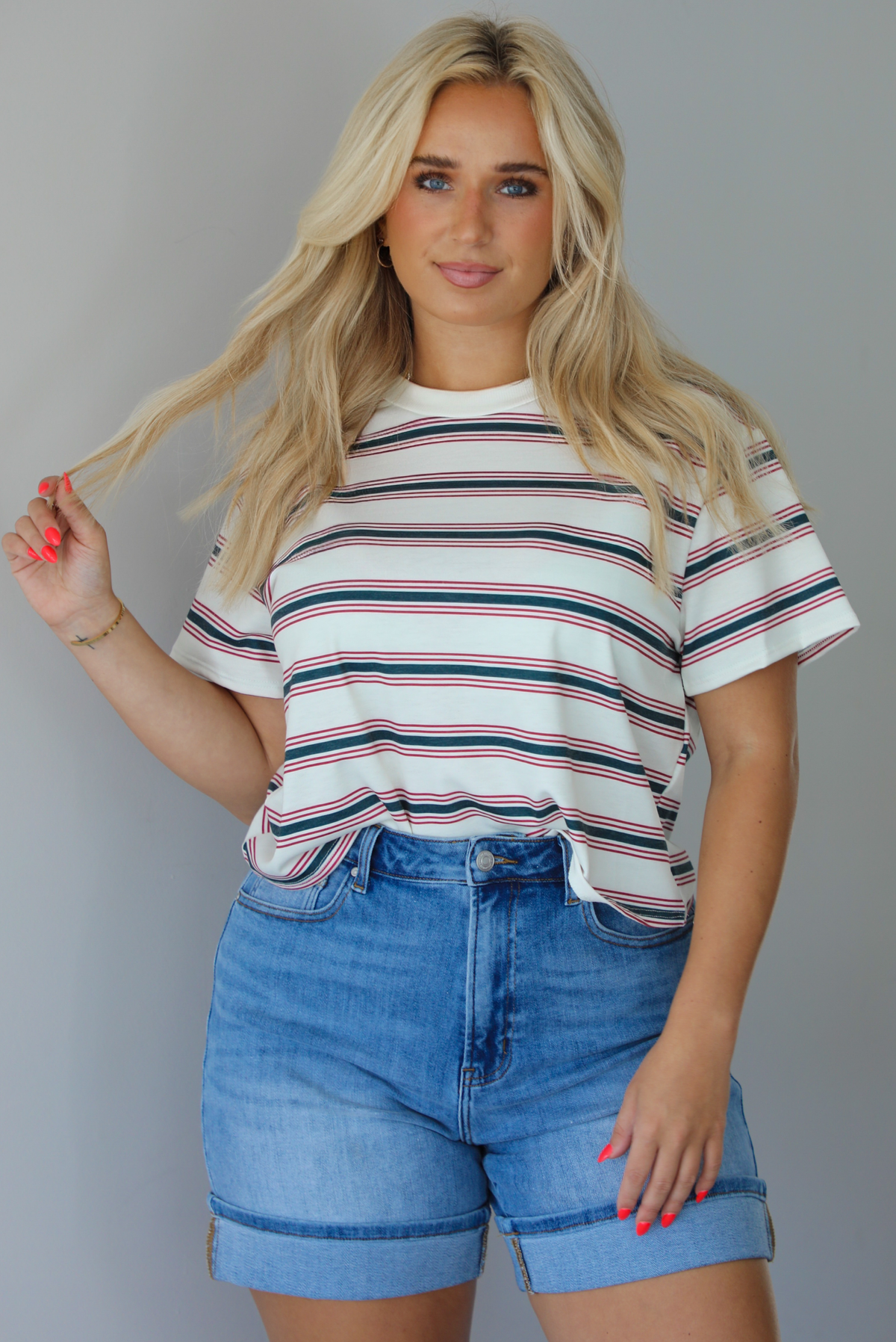 Woman wearing a striped, slightly cropped tee with light-wash denim shorts indoors against a white wall.
