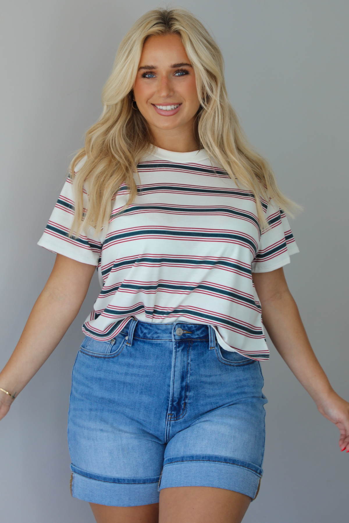 Woman wearing a striped, slightly cropped tee with light-wash denim shorts indoors against a white wall.