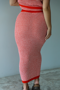 Woman wearing a red and white knit two piece set featuring a sleeveless top and high waisted midi length skirt indoors against a white wall with white marble flooring. The photo shows a closeup of the back of the skirt. 