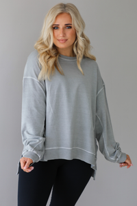 Woman wearing a grey oversized sweater with black leggings that have a slightly flared hem with split hem details in the front. The photo shows a closeup of the sweater and has a white background. 