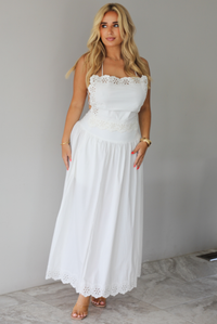 Woman wearing a two piece white set indoors against a white wall with white marble flooring. 