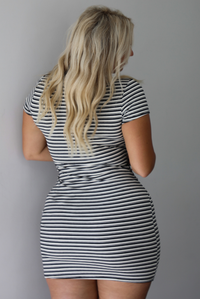 A woman shown from behind wearing a black and white striped fitted mini t-shirt dress featuring a high neckline, short sleeves, with a mini length, standing indoors against a white wall. 