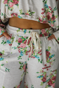 Woman wearing an oatmeal colored and multi-colored floral print two piece set featuring a collared long sleeved crop top and high waisted pants. The photo shows a closeup of the waistline of the bottoms, focusing on the elastic and drawstring waistline.