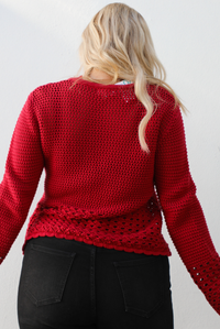 Back of a woman model wearing a burgundy knit cardigan with button closures in the front and black denim jeans. The photo is taken outdoors against a white wall. 