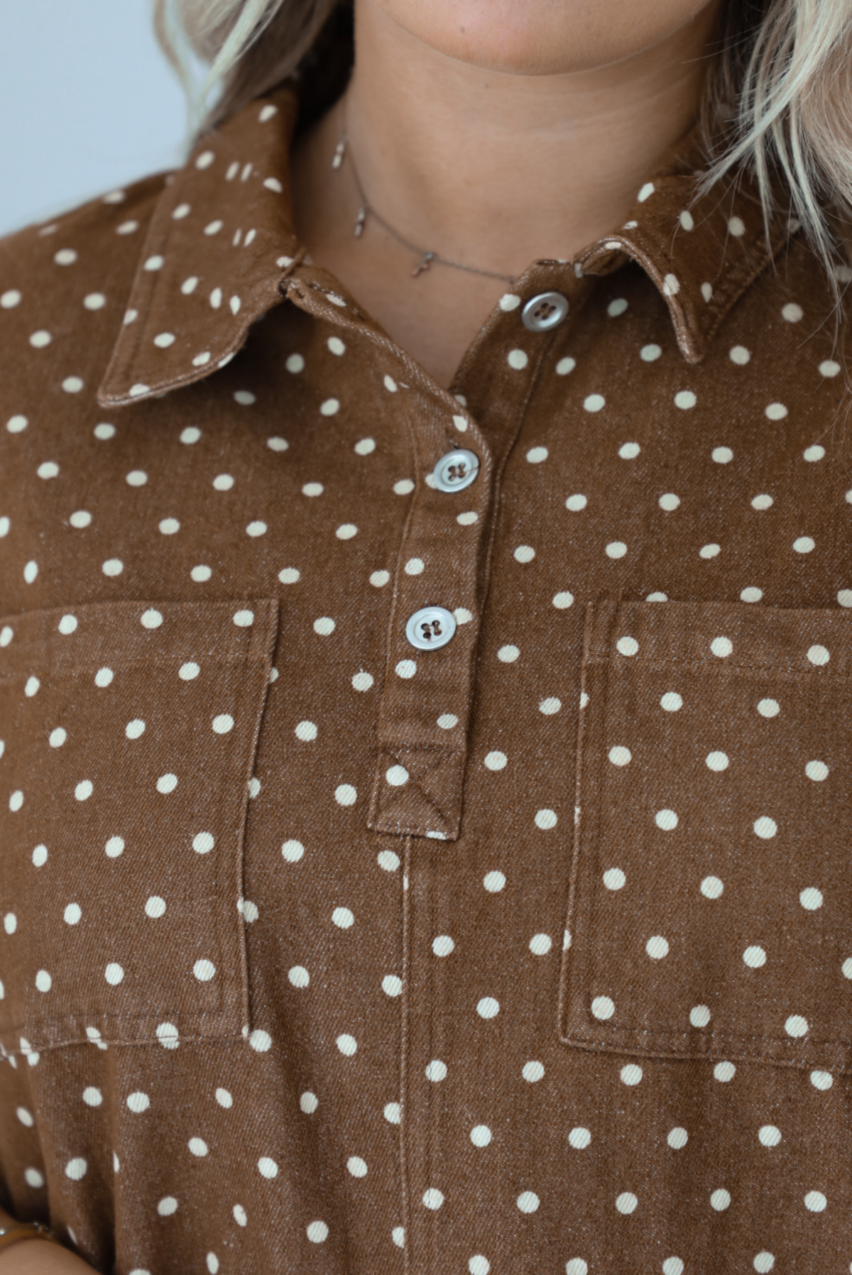 Close-up of a person wearing a brown button-front dress with cream polka dots and two chest pockets.